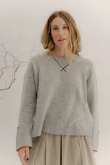 Buzo de lambswool color beige, con escote redondo y detalle en V. Presenta cierres metálicos en los puños que revelan un interior en contraste de color marrón y ribete rojo. Tiene tajos laterales para mayor comodidad y un fit amplio.
