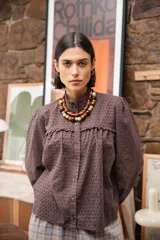Camisa de broderie color chocolate, con cuello alto con volados, cierre frontal de botones y mangas largas con volumen.