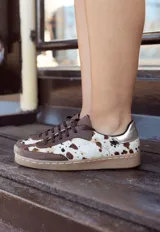 Zapatilla urbana de cuero vacuno con paneles de cuero de pelo con estampado animal print. Presenta detalles en cuero liso color marrón, talón en tono metalizado y suela de goma cosida.