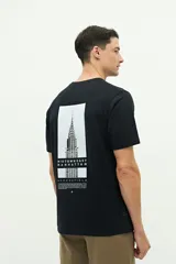 Remera de manga corta color beige con estampado gráfico en la espalda que representa el edificio Chrysler de Nueva York y texto descriptivo.