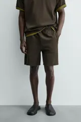Bermuda de hombre color verde oscuro, de corte relajado y tiro medio. Confeccionada en tejido texturado, presenta cintura elástica con cordón de ajuste interno y bolsillos laterales y trasero de vivo.