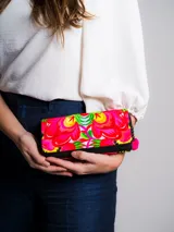Billetera rectangular con cierre de cremallera, confeccionada en tela bordada con diseño floral en tonos fucsia, amarillo, verde y blanco.