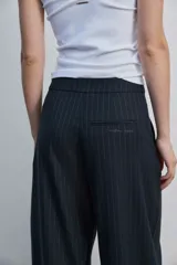 Pantalón de vestir de corte ancho y relajado, color negro con sutiles rayas diplomáticas verticales. Presenta bolsillos laterales y cierre frontal oculto.