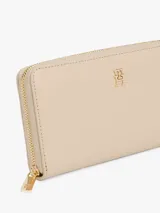 Billetera rectangular color beige, con cierre perimetral de cremallera y logo metálico de monograma TH en el frente.