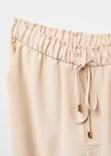 Pantalón recto de corte fluido, color beige, con cintura elástica y lazo ajustable. Cuenta con dos bolsillos laterales y diseño de estilo jogger.