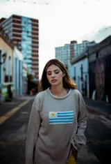 Sweater de hilo de algodón en color beige con diseño tejido de la bandera de Uruguay en el centro. Presenta cuello redondo, mangas largas y un corte holgado.