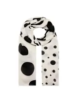 Fular fluido color blanco con estampado de lunares negros y terminaciones deshilachadas.