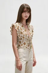 Blusa de diseño estampado con motivos florales y cachemira en tonos marrones sobre base blanca, con escote en V profundo y doble lazo frontal ajustable. Presenta mangas cortas con volados.