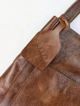 Bolso tipo tote grande de cuero genuino marrón, con asas de hombro dobles, bolsillo exterior con botón a presión y llavero colgante con la marca grabada.