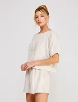 Blusa corta de lino y viscosa color beige, con bordado de grandes flores al tono, cuello redondo, mangas cortas abullonadas y corte holgado.