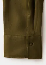 Camisa de lino color verde militar, de corte recto con cuello camisero, manga larga con puños abotonados, bolsillo de parche en el pecho y cierre frontal de botones.
