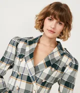 Blazer cropped con estampado de cuadros en tonos verde, blanco y marrón. Tiene cuello solapa, manga larga abullonada y cierre abotonado frontal.