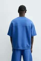 Sudadera de manga corta color marrón oscuro, con cuello redondo y bajo acabado en rib. Presenta un corte relajado y holgado (boxy fit).