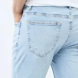 Pantalón de jean corte slim, color azul claro con efecto lavado, cierre frontal con botón y cremallera, y bolsillos laterales y traseros.