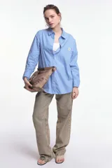 Camisa oversize de popelina a rayas celestes y blancas, con cuello camisero, manga larga con puños abotonados, cierre frontal con botones y un bolsillo en el pecho con etiqueta bordada.