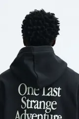 Canguro negro con capucha y bolsillo frontal tipo canguro. Presenta un estampado gráfico en el pecho con el logo de la serie Stranger Things y una silueta del Mind Flayer sobre un atardecer.