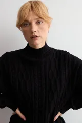 Polerón de punto negro con cuello alto y diseño de trenzas verticales en el frente. Posee mangas largas con puños acanalados y un corte holgado.