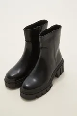 Bota de caña media en cuero sintético color negro, con suela track dentada y cierre lateral interno.