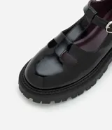 Mocasín estilo Mary Jane de Satinato, confeccionado en poliuretano con acabado brillante. Presenta recortes redondeados en la parte superior, tira ajustable con hebilla metálica y una robusta suela track dentada.