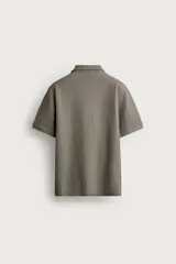 Remera polo regular fit de color gris oscuro, confeccionada en tejido de algodón con textura de rayas verticales. Cuenta con cuello solapa, cierre frontal con botones y mangas cortas con terminación en rib.