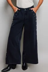 Pantalon de tiro bajo y pierna ancha confeccionado en denim negro con efecto vintage, decorado con ojales metálicos a lo largo de los laterales y los bolsillos.