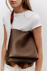 Bolso de hombro tipo saca en color marrón, con diseño minimalista y cierre de clip metálico. Incluye una correa de hombro con detalles troquelados en contraste y herrajes dorados.