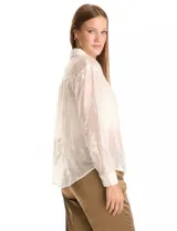 Camisa de tencel color blanco roto, semitransparente, con bordados florales en blanco. Tiene cuello con solapa, cierre frontal con botones decorados y un bolsillo en el pecho.