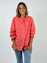 Camisa de algodón con diseño de broderie, color coral, con cuello camisero, cierre frontal de botones y mangas largas con volados en los puños.