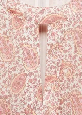 Vestido corto de tejido fluido con estampado paisley en tonos rosados y beige. Presenta cuello redondo con pequeña abertura frontal, mangas largas abullonadas con lazos ajustables en los puños y aberturas laterales en la cintura.