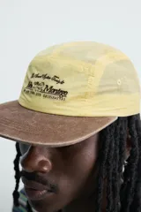 Gorra de 5 paneles de color amarillo claro con tejido ripstop, visera plana marrón de efecto desgastado y bordado frontal en negro. Cuenta con ajuste en la parte posterior.
