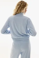 Campera corta de velour color celeste claro, con cuello elevado, cierre frontal y bolsillos insertados. Presenta elástico fruncido en puños y bajo.