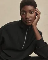 Buzo deportivo negro de corte oversize, confeccionado en tejido DoubleSoft®. Presenta cuello con paneles, media cremallera metálica y puños y bajo amplios.