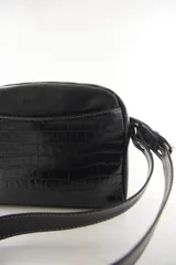 Bandolera semirrígida Sagali de cuero vacuno color bordó, con textura de cocodrilo en el bolsillo frontal y cuerpo liso. Cuenta con cierre superior y correa regulable.