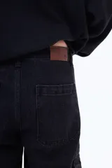 Pantalón cargo de denim negro con corte holgado, bolsillos laterales con solapa y cierre frontal con botón.
