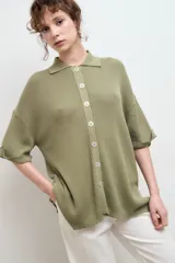 Camisa negra de tejido de punto acanalado, con cuello tipo polo y botones blancos.