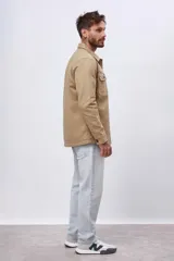 Chaqueta tipo sobrecamisa de algodón color camel, con cuello camisero, cierre frontal de botones oscuros y dos bolsillos de parche con solapa en el pecho.
