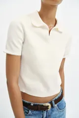 Top de punto color blanco marfil con cuello polo y manga corta. Presenta detalle de puntilla con forma de onda en el cuello y los puños.