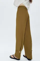 Pantalón de tiro alto con corte recto, cierre frontal con cremallera y botones decorativos en el bajo.