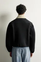 Cazadora boxy fit de tejido técnico negro con mezcla de algodón, de corte corto, manga larga con puños abotonados y cierre frontal con cremallera oculta. Cuenta con cuello solapa desmontable en tejido combinado color beige a contraste y bolsillos de vivo en la cadera.