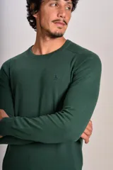 Sweater de punto fino color verde oscuro, con cuello redondo, mangas largas y puños y ruedo acanalados. Presenta un pequeño logo bordado en el pecho.