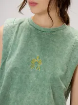 Musculosa crop de algodón con efecto acid wash en color lila, cuello redondo, hombreras marcadas y pequeño bordado central en el pecho.