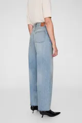 Pantalón de jean celeste de tiro alto, corte holgado y pierna ancha con dobladillo sin rematar. Presenta cierre con botones, diseño de cinco bolsillos y detalle de costura suelta en el interior de la pierna.