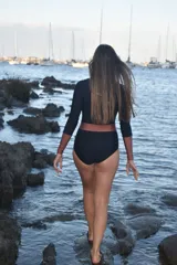 Traje de baño enterizo de manga larga en color negro con detalles en color cobre en la cintura y los puños. Presenta un cierre frontal y diseño de corte clásico.