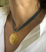 Gargantilla con cinta de terciopelo gris y dije dorado con la imagen de la Virgen de Guadalupe.