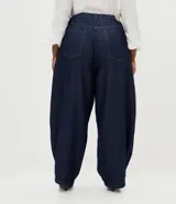 Pantalón de jean raw azul oscuro, corte barrel con piernas anchas y cintura cónica. Presenta costuras contrastantes, cierre tradicional con botón y bolsillos laterales.