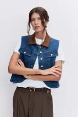Chaleco de denim azul con cuello camisero en contraste color marrón, cierre frontal con botones metálicos y bolsillos superiores con solapa.