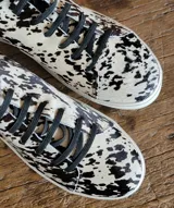 Zapatillas urbanas de cuero con pelo, estampado animal print tipo vaca en blanco y negro, con cordones negros y suela de goma blanca.