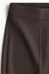 Pantalón sastrero de tiro alto y piernas amplias, color marrón, con pliegues frontales y traseros.