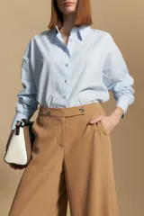 Pantalón ancho color tostado, de silueta fluida y cintura elastizada. Presenta una pretina ancha con botones metalizados irregulares.