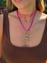 Collar con cordón ajustable color beige y dije de sol plateado.